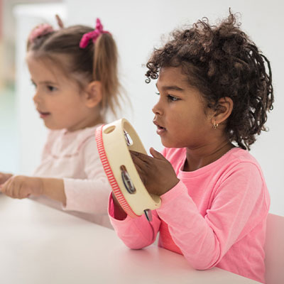 Two young girls wearing pink playing tambourine in ECM class 400px