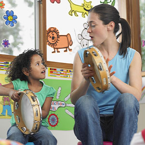Female early childhood music teacher and young student playing tamborines