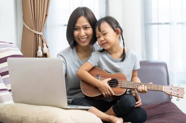 Mom on her laptop and daughter playing ukulele