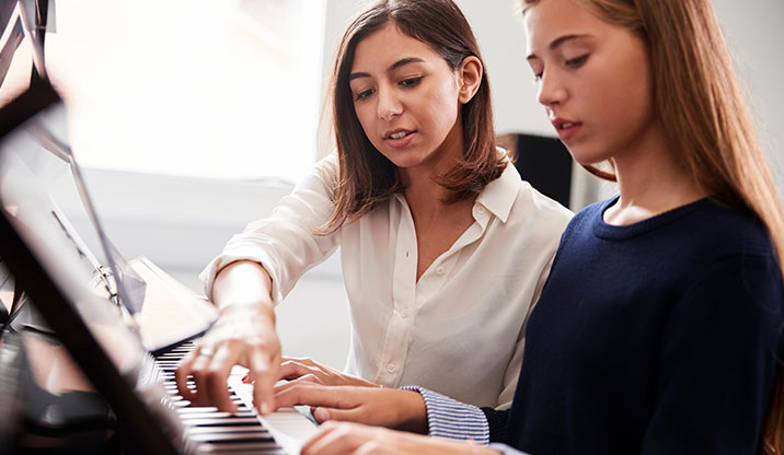 Female teacher helping young female student at the piano 