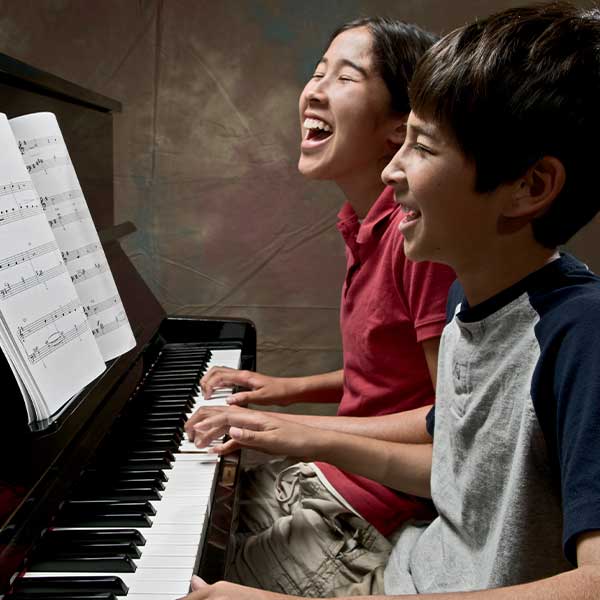 Two students laughing at a piano 600px