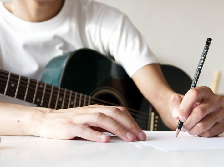 Person holding an accoustic guitar and writing music 716x498px