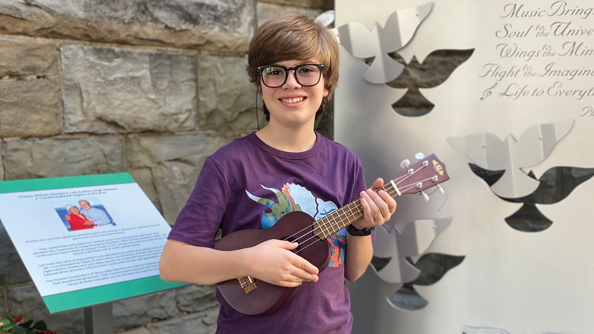 Isaac smiles at the camera while he plays the ukulele in the Conservatory courtyard