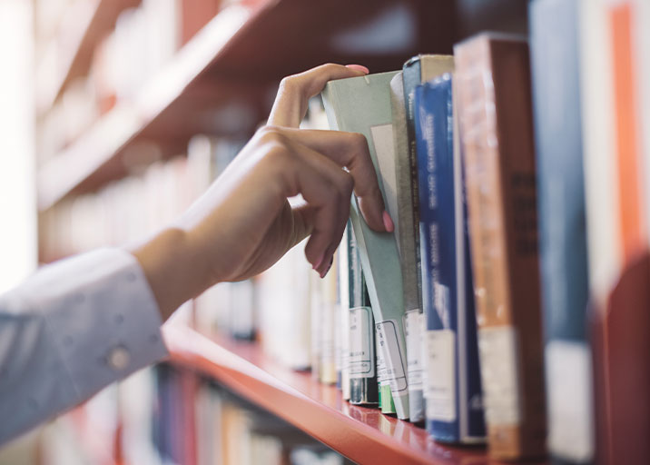 Hand removing library book from a shelf 716x512px