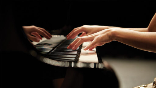 Hands playing a grand piano with a dark background