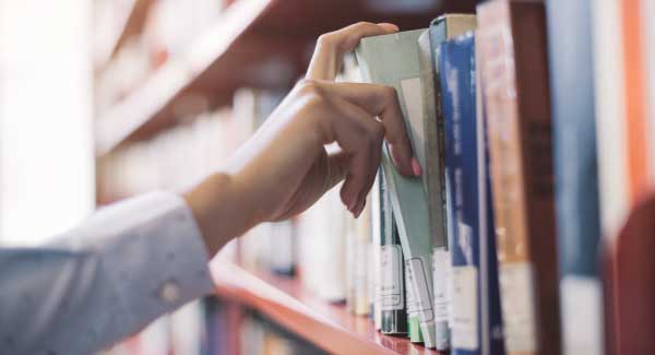 Hand removing library book from a shelf 325x600px