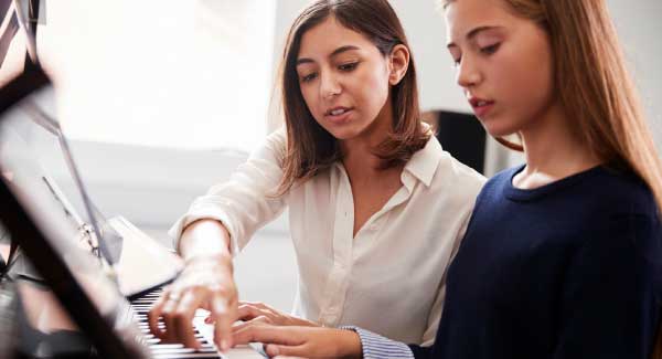 Female instructor helps female student with her piano lesson